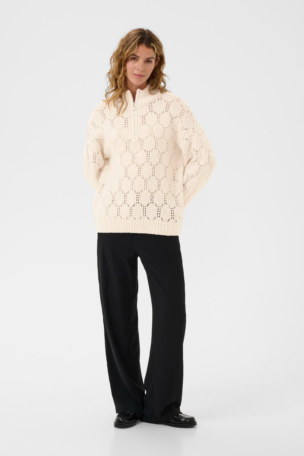 Woman wearing a cream-colored sweater with a geometric pattern on a white background