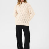 Woman wearing a cream-colored sweater with a geometric pattern on a white background