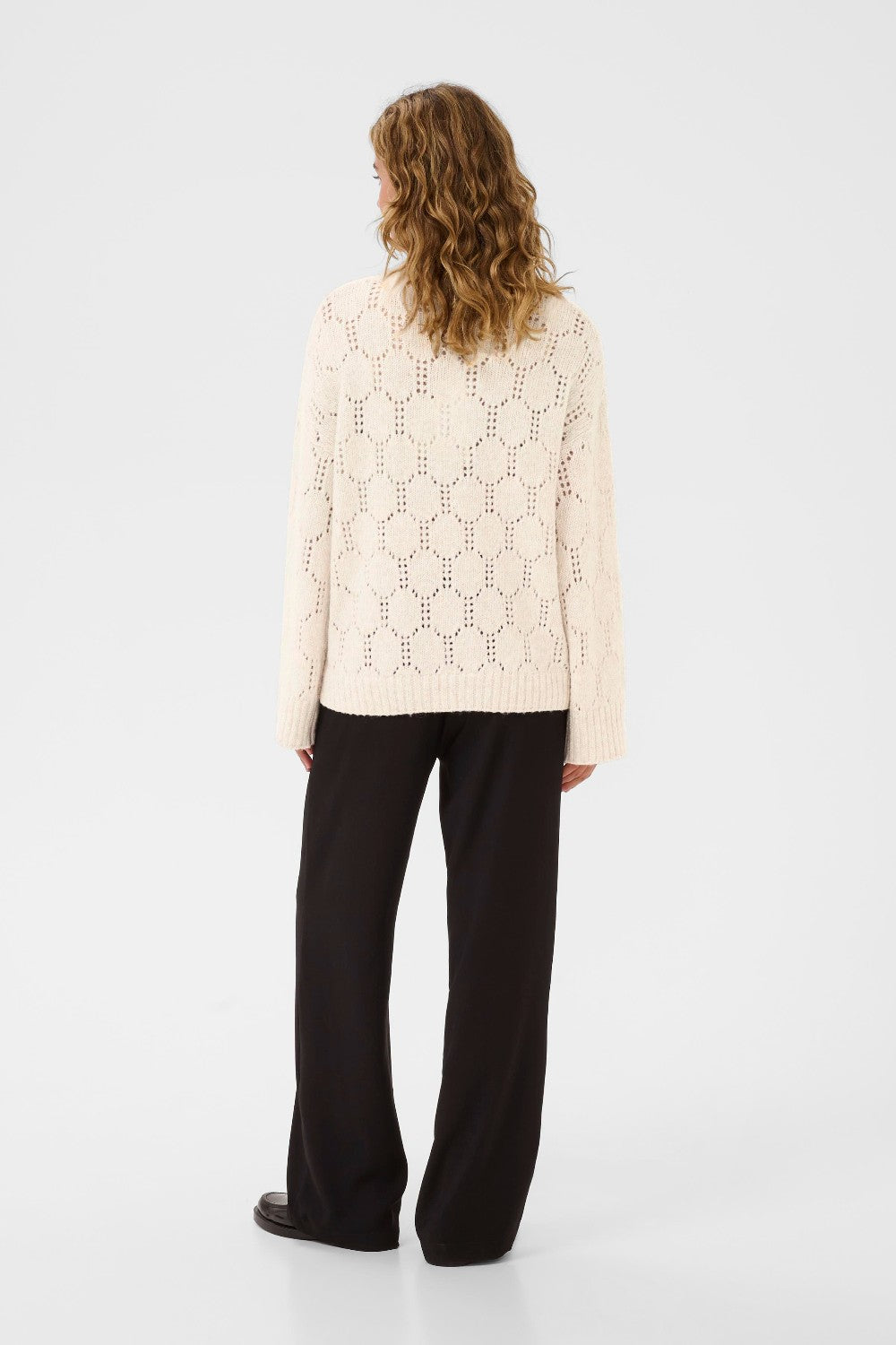 Person wearing a light-colored patterned sweater and black pants on a white background