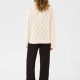 Person wearing a light-colored patterned sweater and black pants on a white background