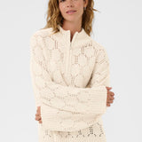 Woman wearing a cream knitted sweater against a plain background