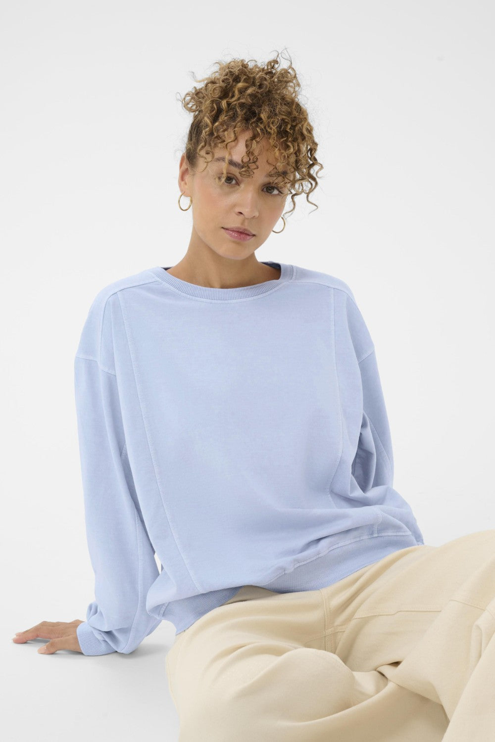 Woman wearing a light blue sweatshirt sitting on a white background