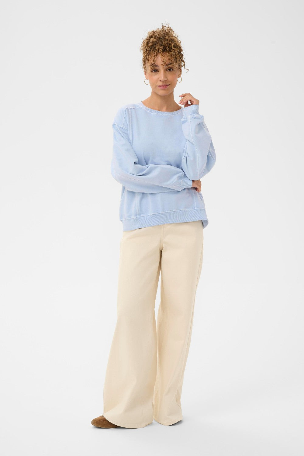 Woman wearing a light blue sweater and beige pants on a white background