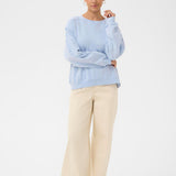 Woman wearing a light blue sweater and beige pants on a white background