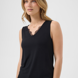 A woman wearing a sleeveless black top with a V-neck and black lace trim, photographed against a light gray studio background.