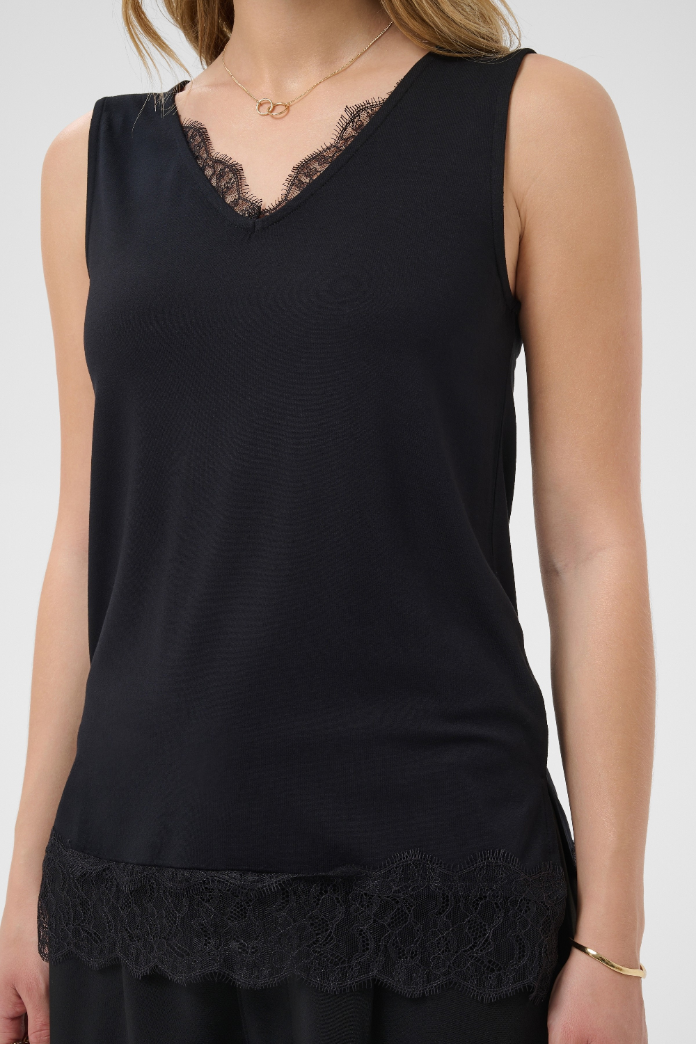 A sleeveless black V-neck top with black lace trim along the neckline and hem, shown on a model against a light gray background.