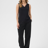 A woman modeling a black sleeveless top with a lace hem and black wide-leg pants, paired with brown ankle boots, against a light gray studio background.