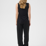 A woman viewed from behind wearing a black sleeveless top and black wide-leg pants, standing against a light gray studio background.