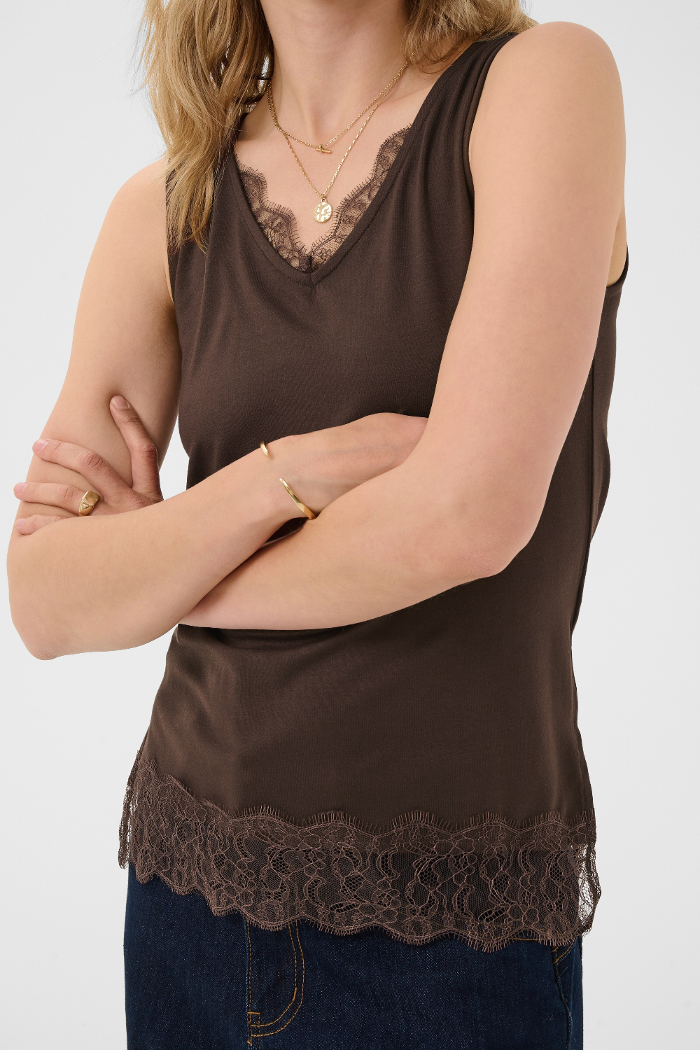 Woman wearing a brown sleeveless top with lace trim on a white background