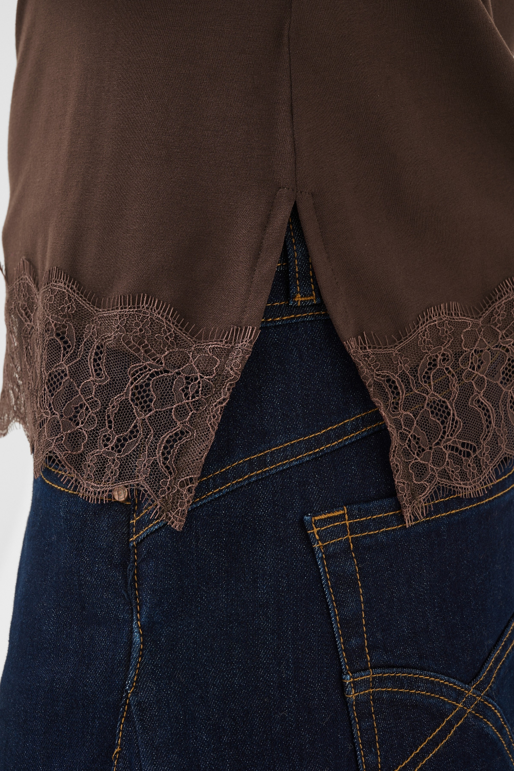 Brown lace-trimmed top over blue jeans on a white background