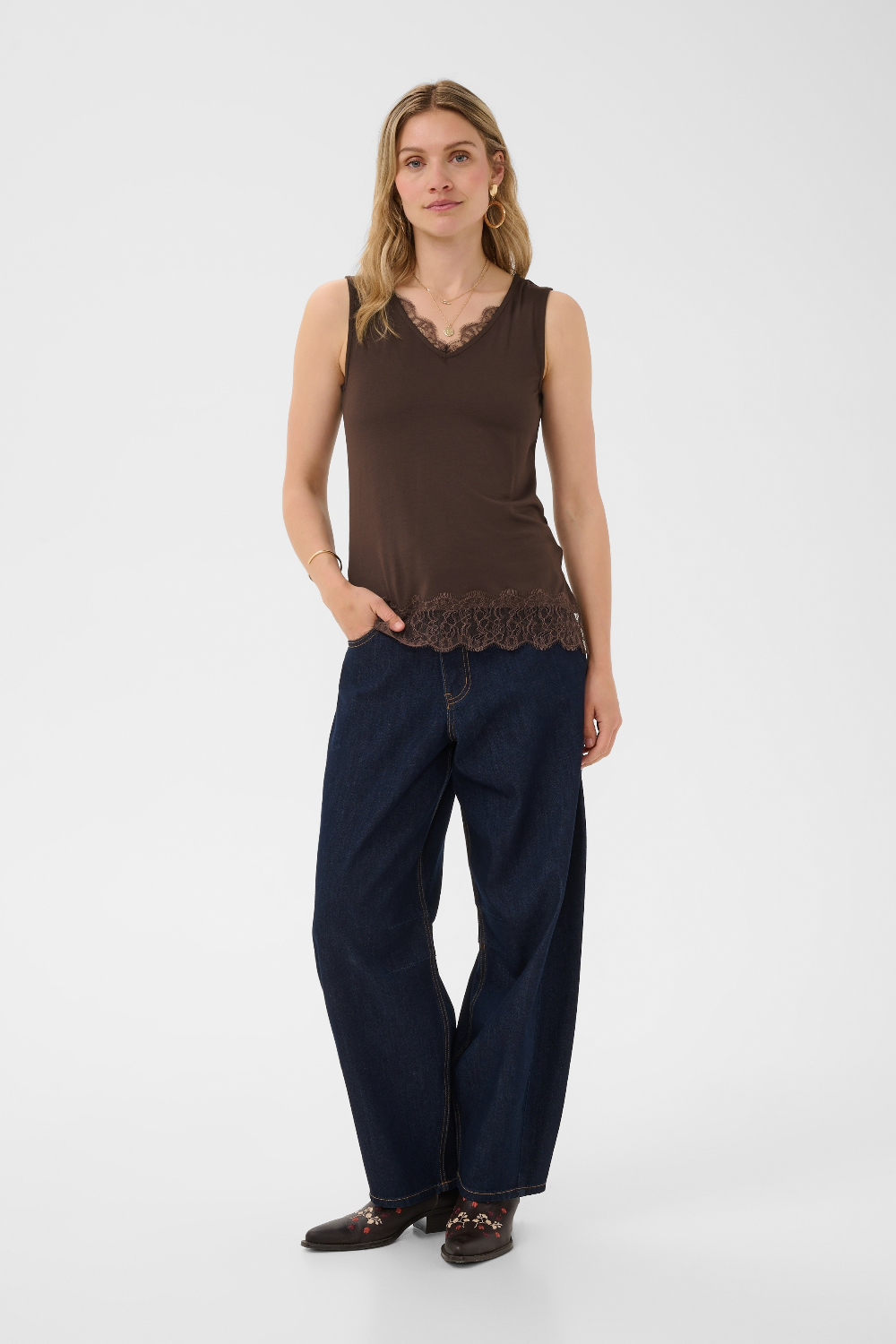 Woman wearing a brown sleeveless top with lace detail and dark blue pants on a white background