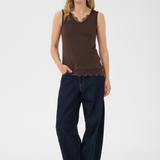 Woman wearing a brown sleeveless top with lace detail and dark blue pants on a white background