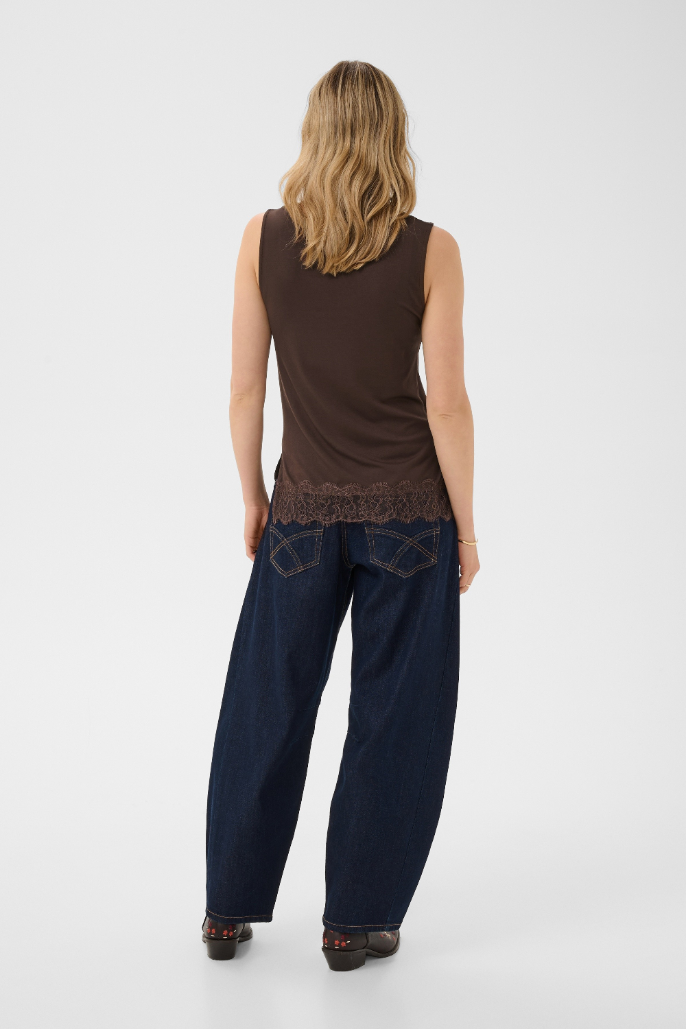Woman wearing a brown sleeveless top and dark blue pants on a white background