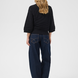 A woman shown from the back wearing a black ribbed knit sweater, dark blue wide-leg jeans with contrast stitching, and tan block-heel boots, against a light gray studio background.