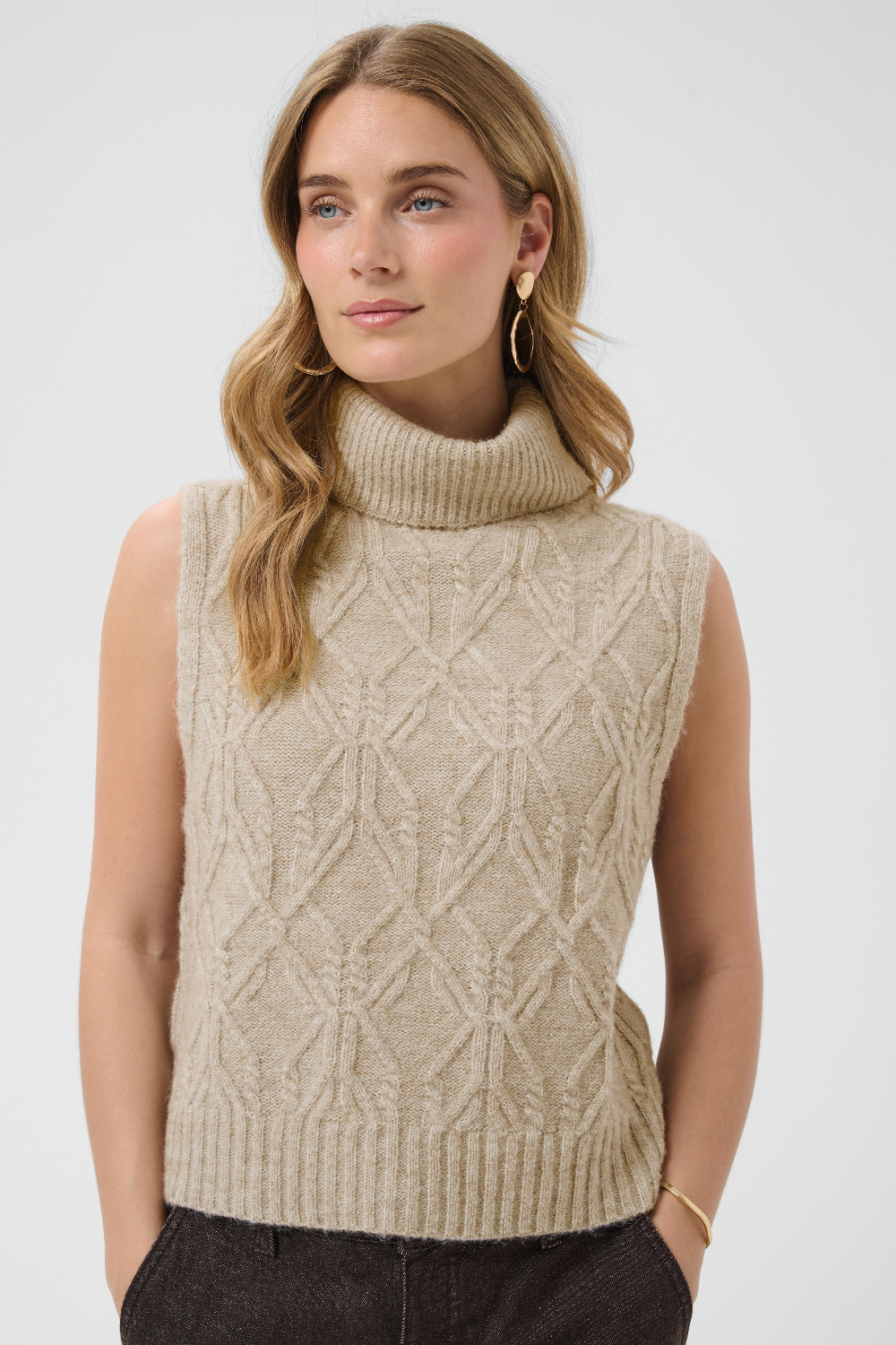 Woman wearing a beige knitted sleeveless sweater against a white background