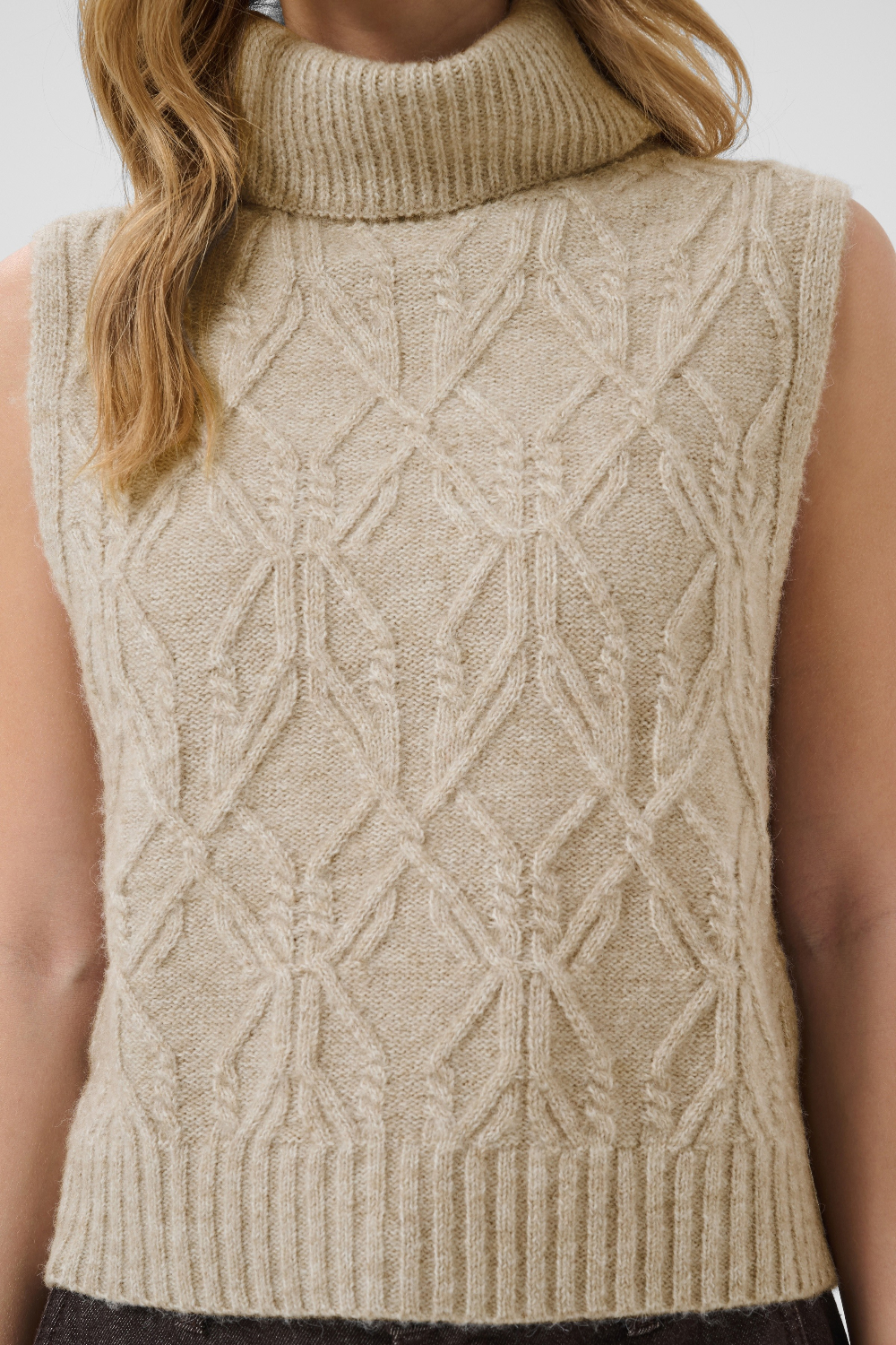 Beige knitted sleeveless sweater with geometric pattern worn by a person.