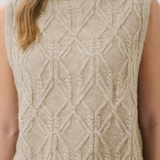 Beige knitted sleeveless sweater with geometric pattern worn by a person.