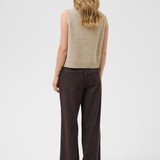 A woman shown from the back wearing a sleeveless beige knit vest and dark brown wide-leg trousers against a light gray studio background.