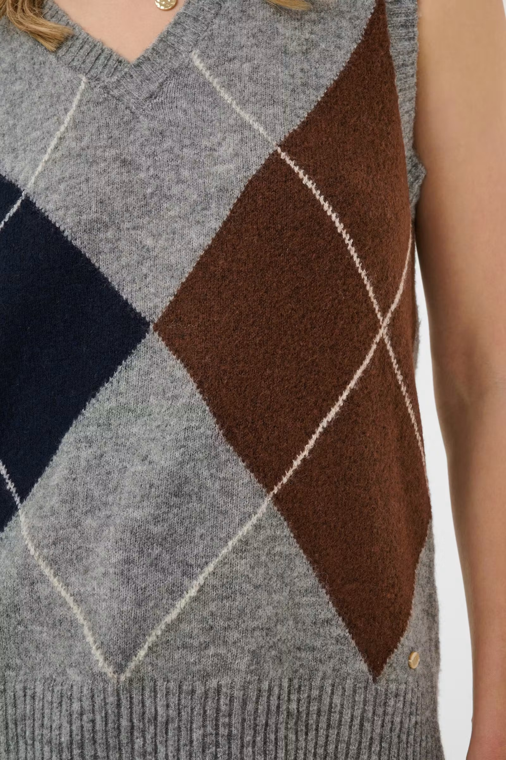 Close up of a sleeveless grey sweater featuring a dark blue and brown argyle design.