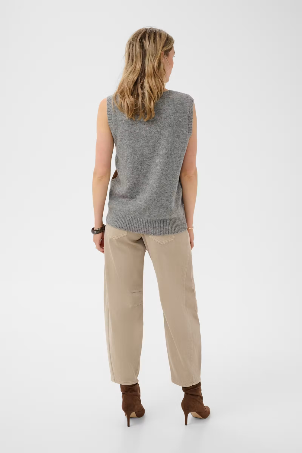 Woman wearing a sleeveless grey sweater with tan pants, shown from the back, against a light background.