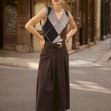 Woman wearing a sleeveless grey sweater featuring a dark blue and brown argyle design with a brown skirt in an outdoor city setting.