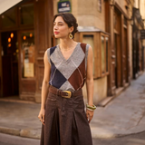 Woman wearing a sleeveless grey sweater featuring a dark blue and brown argyle design with a brown skirt in an outdoor city setting.