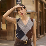 Woman wearing a sleeveless grey sweater featuring a dark blue and brown argyle design with a brown skirt in an outdoor city setting.