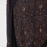 Close-up of a long-sleeve button-front blouse with an intricate paisley and floral pattern in dark brown, rust red, and cream on a black base, worn by a model.