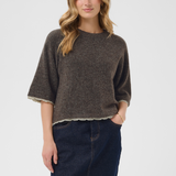 A woman modeling a dark brown heathered knit sweater with a light coloured hem and elbow-length sleeves, paired with a dark blue denim skirt, against a light gray studio background.
