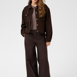 A woman modeling a dark brown cropped jacket and wide-leg pants over a  knit top, photographed against a light gray studio background.