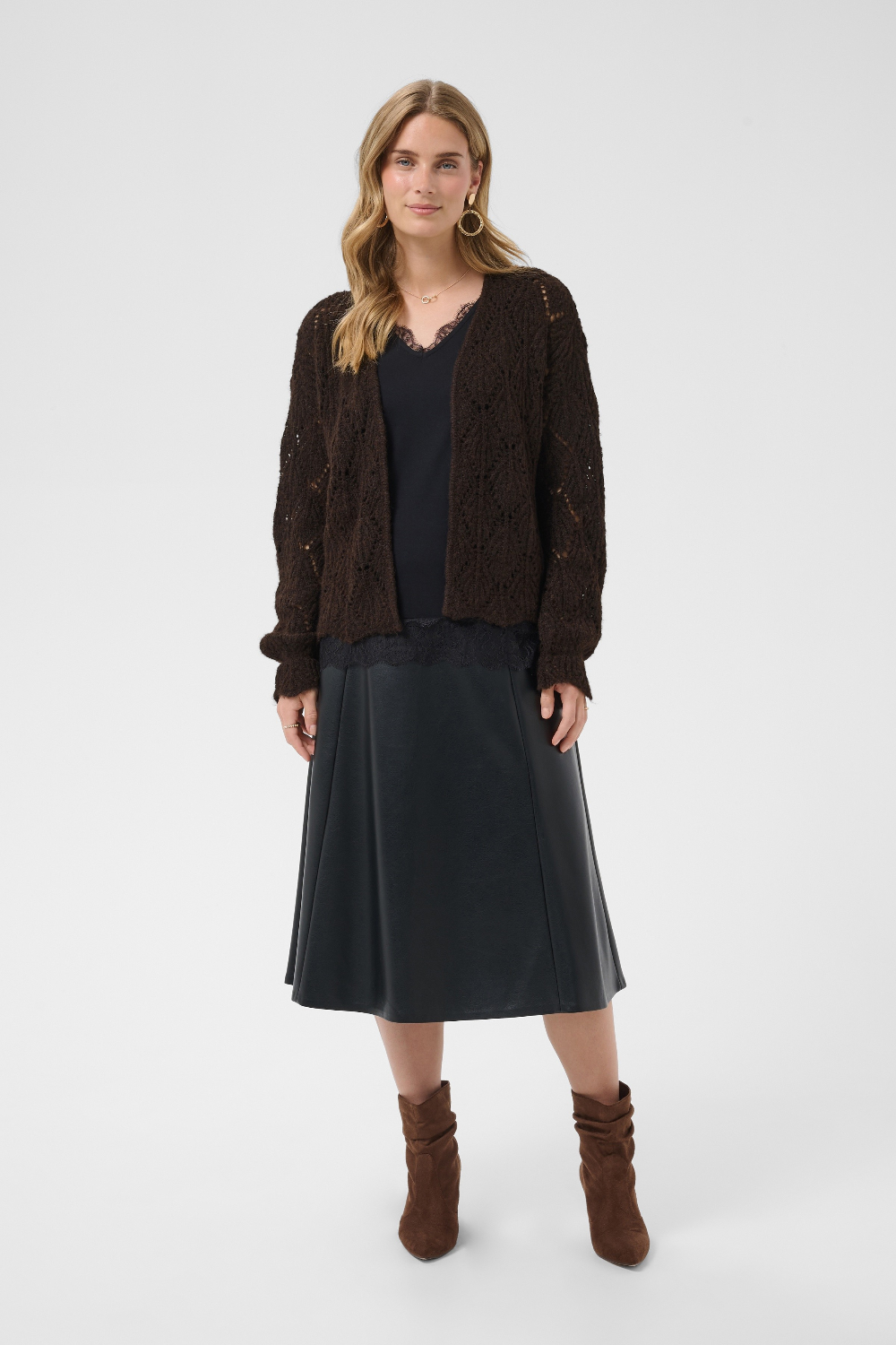 Woman wearing a brown cardigan, black top, black skirt, and brown boots on a white background