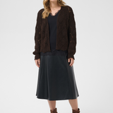 Woman wearing a brown cardigan, black top, black skirt, and brown boots on a white background