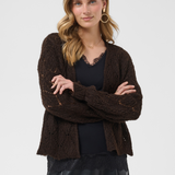 A woman modeling a dark brown open-front knit cardigan with a textured pattern, worn over a black top and black skirt against a light gray studio background.