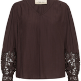 A dark brown crinkled blouse with long sheer sleeves featuring intricate floral lace cuffs, a V-neckline, and a cream-colored neck label that reads 'CREAM'.