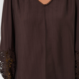 A woman wearing a dark brown long-sleeve blouse with a V-neckline, gathered shoulders, and black lace trim at the cuffs and neckline.
