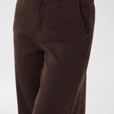 Close up of a person modelling a black sweater and a brown trouser style denim against a light backdrop.