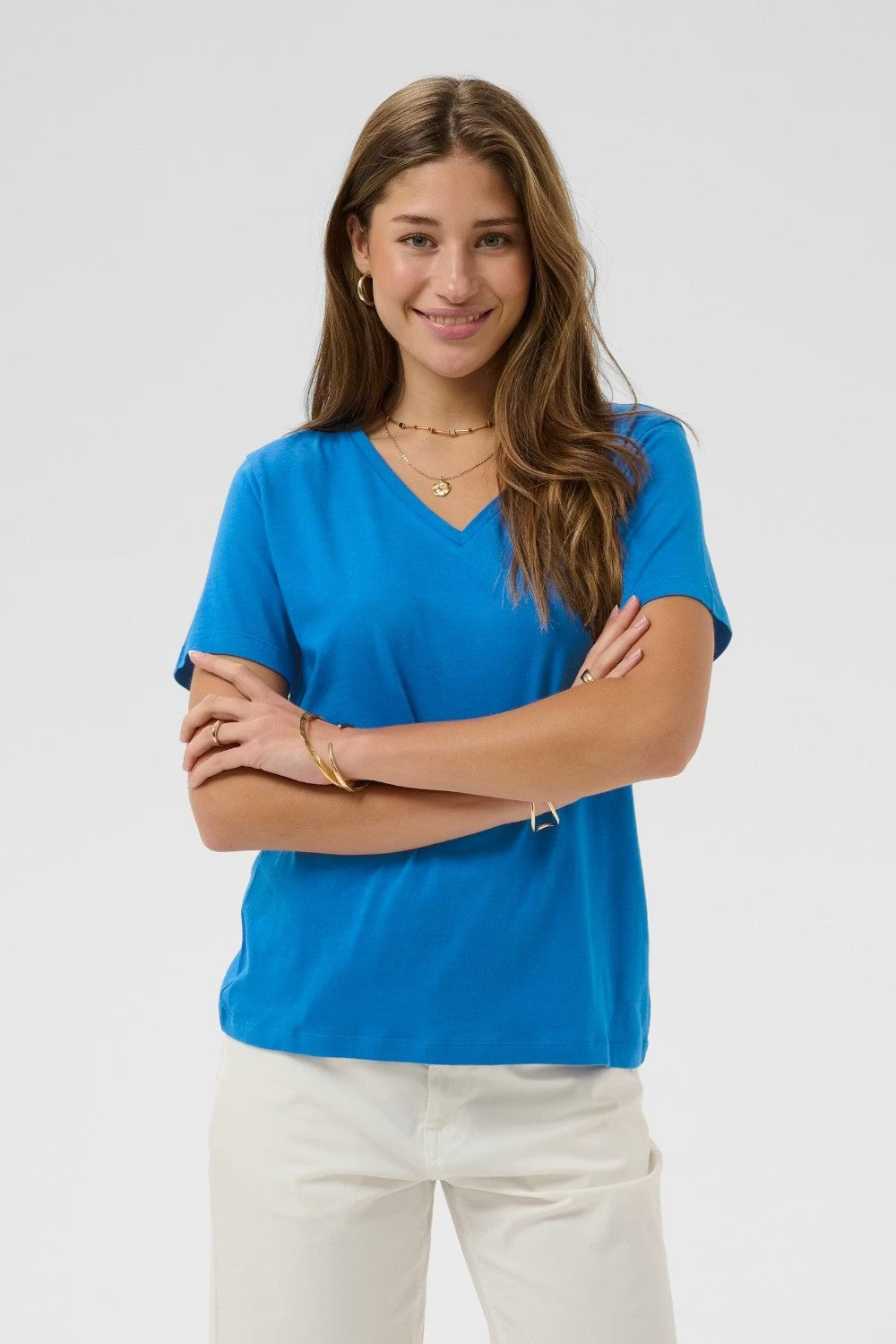 Woman wearing a blue shirt and white pants against a plain background