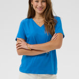 Woman wearing a blue shirt and white pants against a plain background