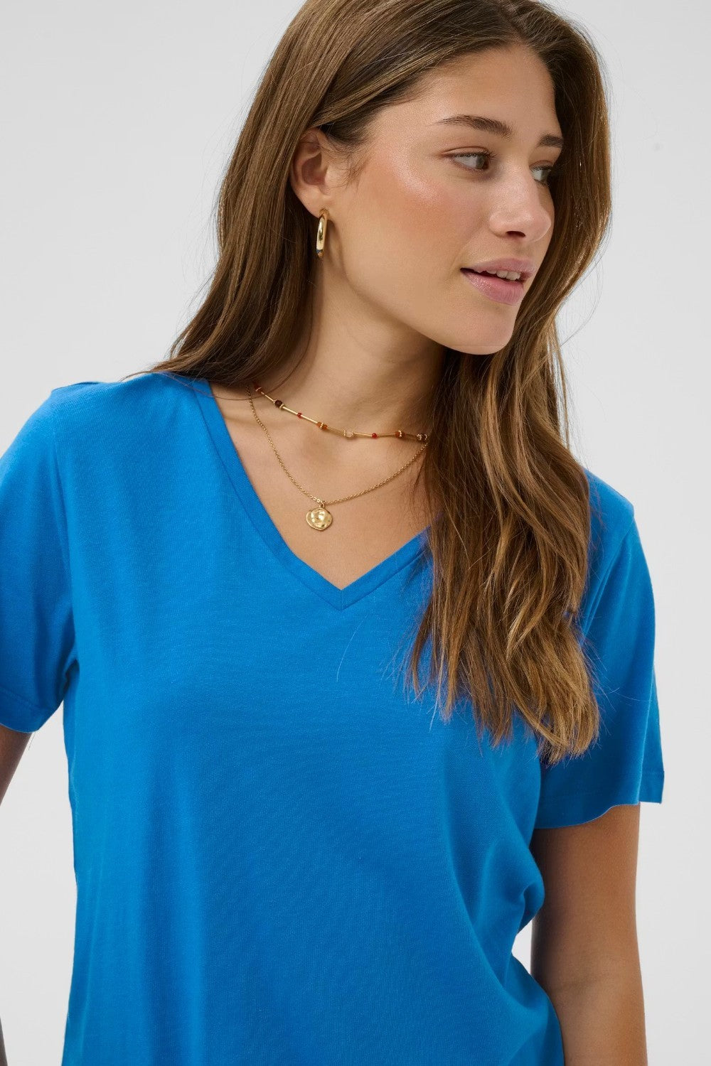 Woman wearing a blue shirt and gold necklaces on a white background