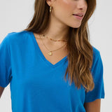 Woman wearing a blue shirt and gold necklaces on a white background