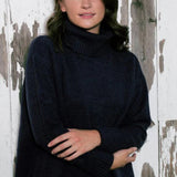 Woman wearing over sized black turtle neck sweater standing in front of a distressed wood wall.