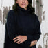 Woman wearing over sized black turtle neck sweater standing in front of a distressed wood wall.