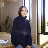 Woman wearing a navy blue sweater sitting on a wooden bench indoors.