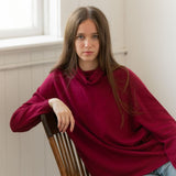 Woman sitting on a wood chair wearing loose red sweater and blue jeans.