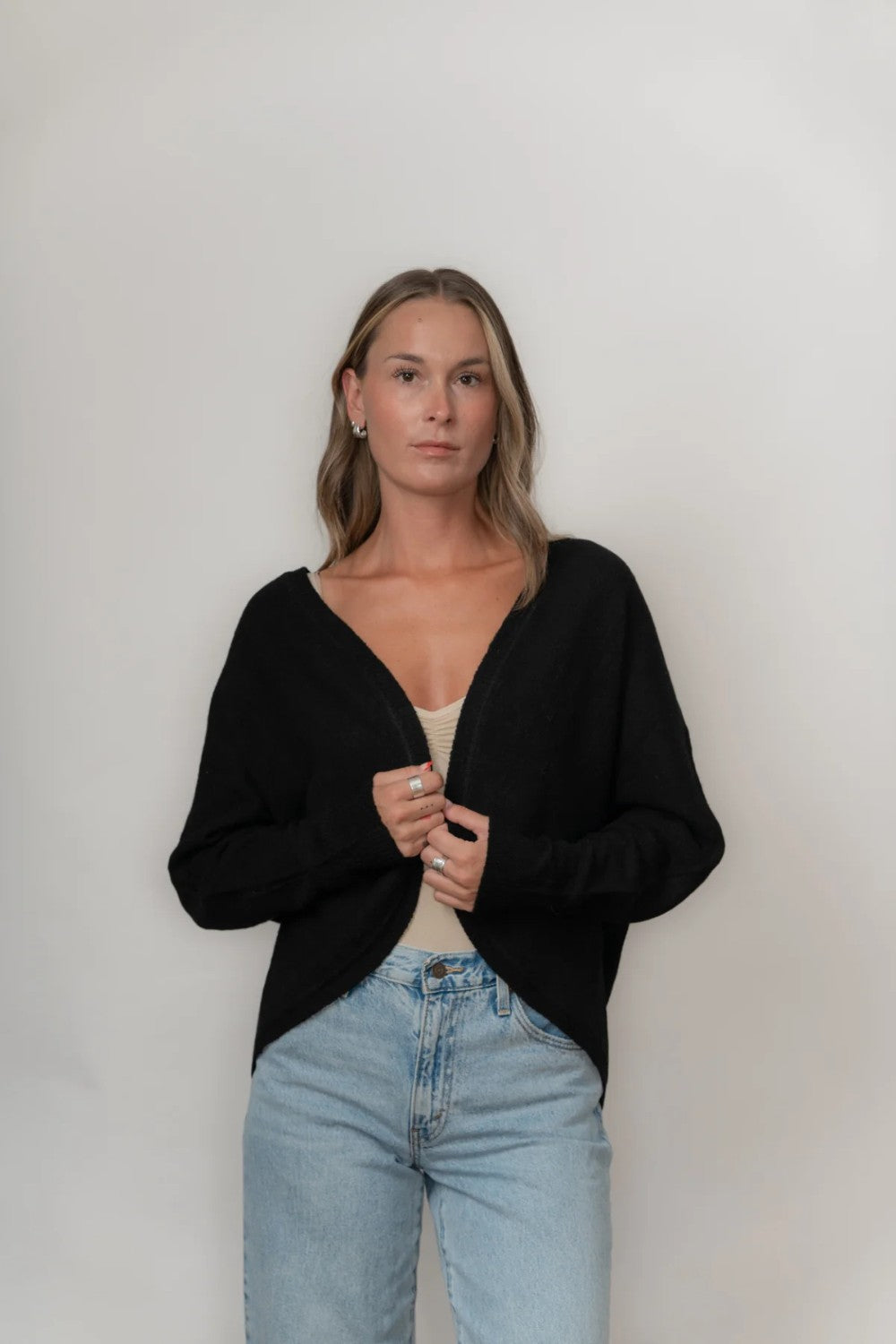 Woman wearing a black cardigan and light blue jeans against a plain background