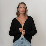 Woman wearing a black cardigan and light blue jeans against a plain background