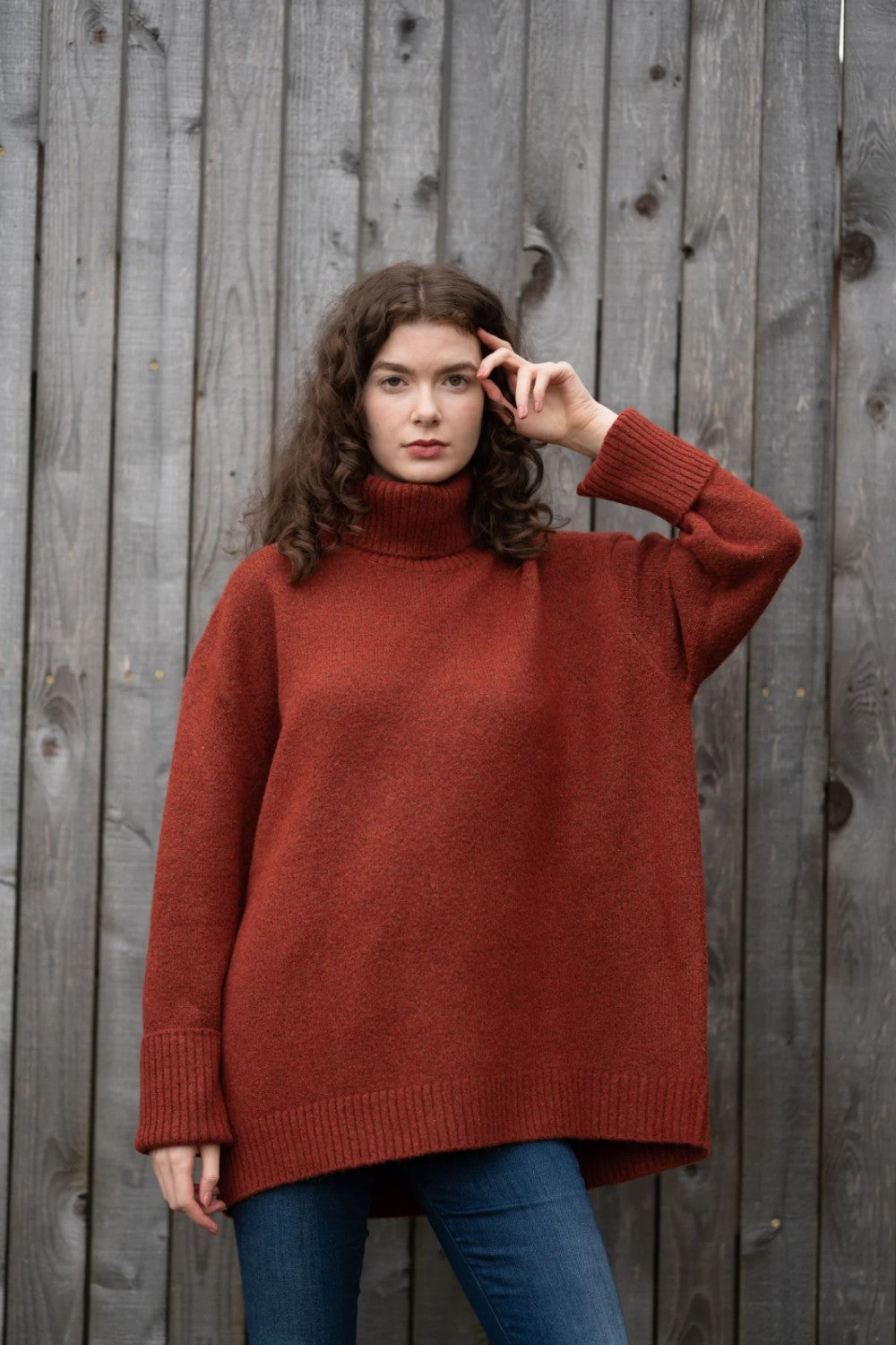 Woman wearing an oversized orange turtle neck sweater standing in front of a wooden fence.