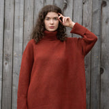 Woman wearing an oversized orange turtle neck sweater standing in front of a wooden fence.