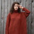 Woman wearing an oversized orange turtle neck sweater standing in front of a wooden fence.
