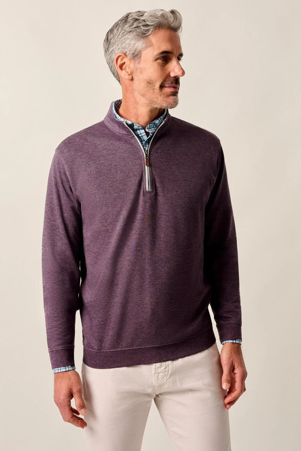Man wearing a purple quarter-zip sweater with a patterned shirt underneath on a beige background